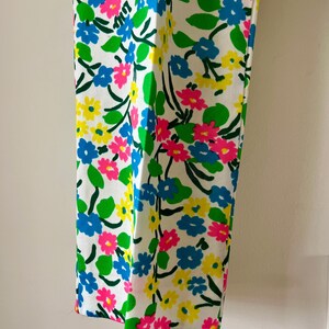 Puede incluir: Pantalones blancos con un vibrante estampado floral. El dise&ntilde;o presenta flores azules, rosas y amarillas con hojas verdes sobre un fondo blanco. Los pantalones tienen un corte de pierna recta y un dise&ntilde;o colorido y llamativo.