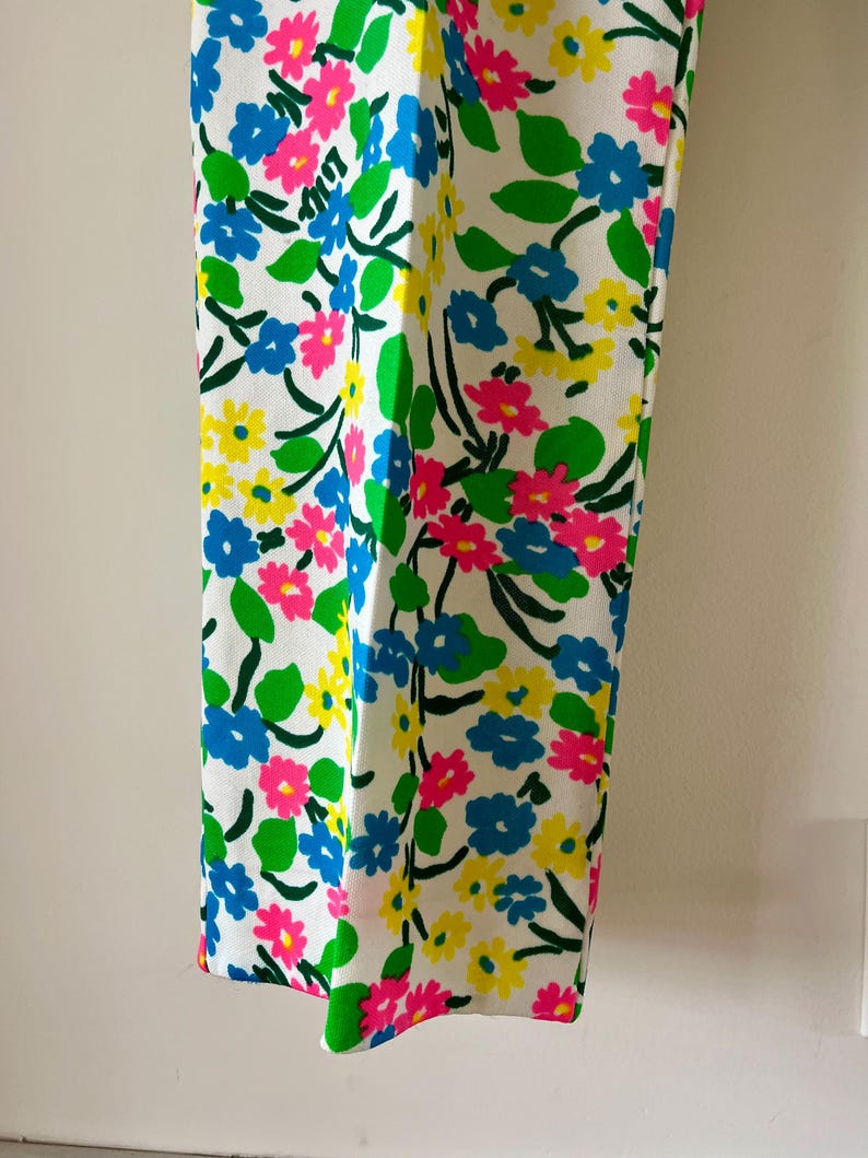 Puede incluir: Pantalones blancos con un vibrante estampado floral. El dise&ntilde;o presenta flores azules, rosas y amarillas con hojas verdes sobre un fondo blanco. Los pantalones tienen un corte de pierna recta y un dise&ntilde;o colorido y llamativo.