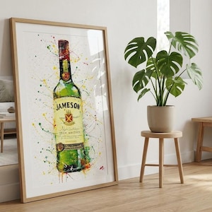 May include: A framed art print showing a watercolour illustration of a Jameson Irish Whiskey bottle. The green bottle has a red cap and a yellow label. The artwork includes colourful paint splatters and is in a light wood frame.