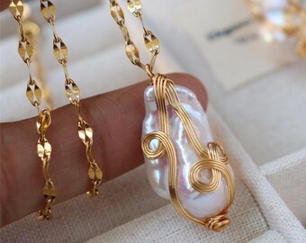 May include: A gold-colored necklace with a large, irregularly shaped white pearl pendant, wire-wrapped in gold. Matching gold earrings with similar pearl drops are also visible. The jewelry is displayed in a white jewelry box.