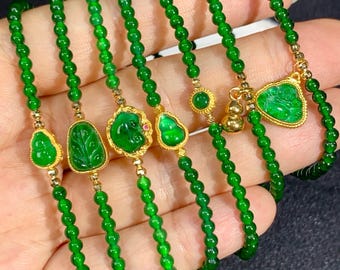 May include: A collection of green jade bracelets with gold accents. Each bracelet features small, round jade beads strung together. Some bracelets have gold pendants with carved jade designs, including a heart, a leaf, and a round shape.