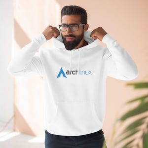 Puede incluir: Sudadera con capucha blanca con bolsillo de canguro. La parte delantera presenta el logotipo azul y blanco "arch linux". La sudadera está hecha de un material suave y tiene una capucha con cordón.