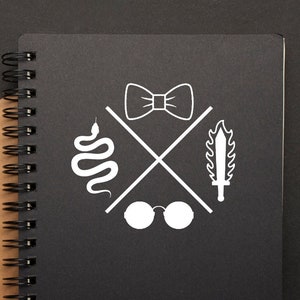 May include: A black spiral notebook with a brown cover. The notebook has a white design on the front cover featuring a snake, glasses, a bow tie, and a sword.