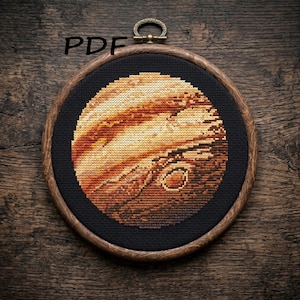 May include: A circular cross-stitch embroidery featuring a detailed depiction of the planet Jupiter in shades of orange, brown, and cream, set against a black fabric background within a round wooden hoop frame. The text PDF is visible.