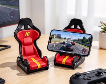 May include: Two racing-style chair phone stands in black and red with yellow stripes. One stand is empty, while the other holds a smartphone displaying a racing game. The empty chair features the number 16 printed in yellow on the headrest.