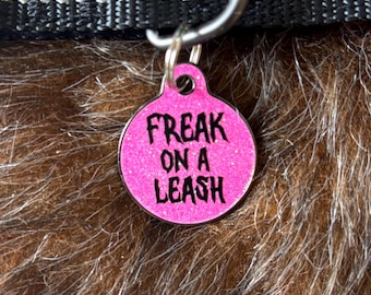 May include: Pink dog tag with glitter and black text that reads "Freak on a leash."