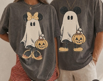 May include: Two charcoal gray short-sleeve t-shirts featuring a distressed graphic print of a ghost character wearing mouse ears and a bow, or mouse ears alone, while holding a jack-o'-lantern pumpkin bucket for a Halloween theme.