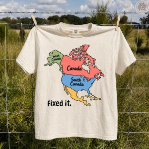 Op de afbeelding: Een crèmekleurig T-shirt met korte mouwen en een kleurrijke kaart van Noord-Amerika. De kaart is verdeeld in secties met de labels West Canada in het groen, Canada in het rood en South Canada in het blauw, met de tekst Fixed it. eronder.