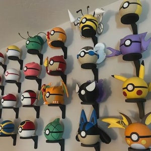 May include: A display of handmade Pokemon-themed wall decorations. The collection features various characters, including Pikachu, in a range of colours, mounted on black brackets against a white wall. Each piece is uniquely designed and crafted.