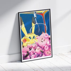 May include: A framed art print featuring a claw machine with a yellow Pikachu and several pink Jigglypuff plush toys. The artwork has a blue background and is leaning against a white wall.