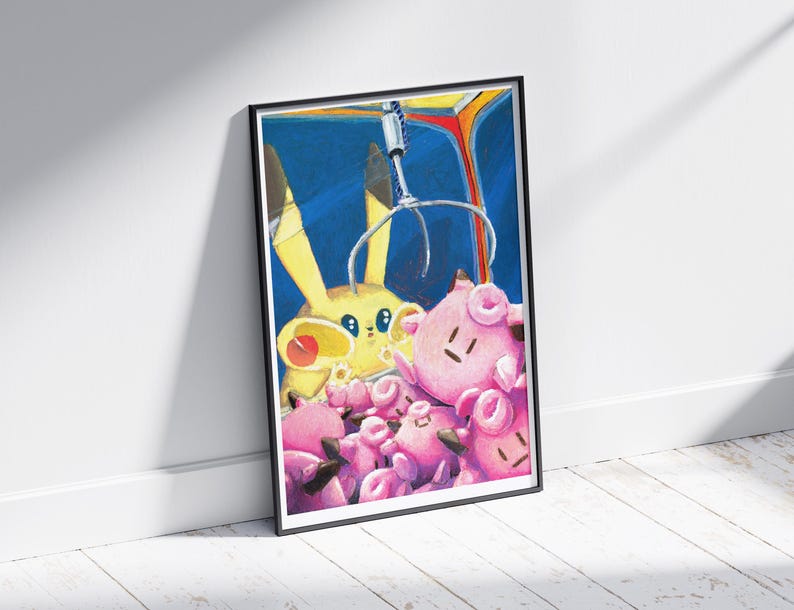 May include: A framed art print featuring a claw machine with a yellow Pikachu and several pink Jigglypuff plush toys. The artwork has a blue background and is leaning against a white wall.