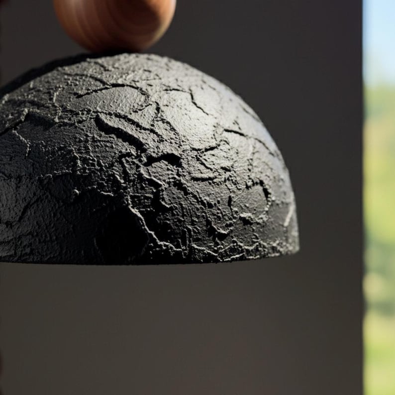 May include: A black, textured, semi-spherical object with a rough, cracked surface. A small, rounded, wooden object rests on top. The background is a dark gray with a glimpse of a green, outdoor scene.