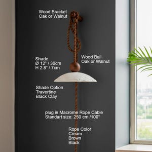May include: A hanging lamp with a cream-colored shade, 12 inches in diameter and 2.8 inches high, suspended by a brown macrame rope. The lamp features a wooden bracket and ball, with options for travertine or black clay shades. The rope is 100 inches long.
