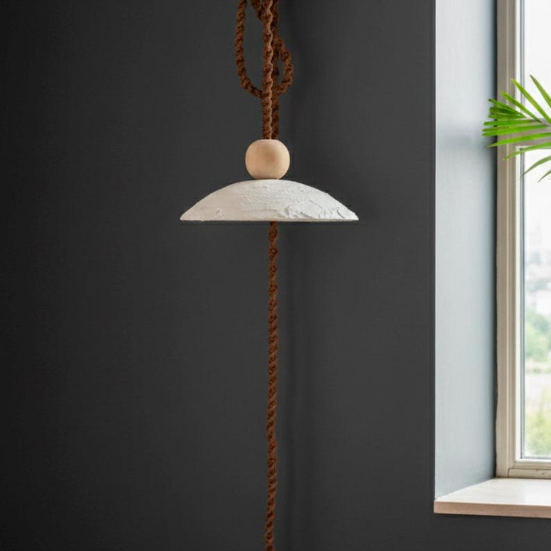 May include: A modern pendant light with a white, textured shade and a wooden sphere accent. The light hangs from a brown, twisted rope. The design is minimalist and suitable for various interior styles.