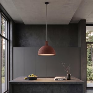 May include: A dome-shaped pendant light with a textured, dark reddish-brown exterior and a smooth white interior. The fixture hangs from a thin black cord attached to a small cylindrical top piece, suspended centrally above a dark grey kitchen island.