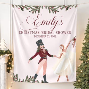 May include: A white fabric backdrop featuring a watercolor illustration of a nutcracker and a bride dancing. The text reads Emily's CHRISTMAS BRIDAL SHOWER DECEMBER 22, 2027. The top and bottom borders are decorated with green holly leaves and red berries.