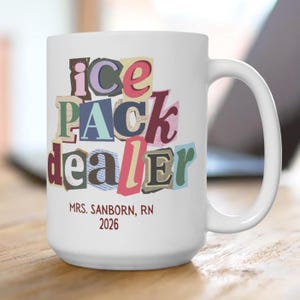 May include: White ceramic mug with the words "ice pack dealer" in a colorful, cut-out letter design. Below the text is "MRS. SANBORN, RN 2026" in a smaller, dark red font. The mug has a large handle.