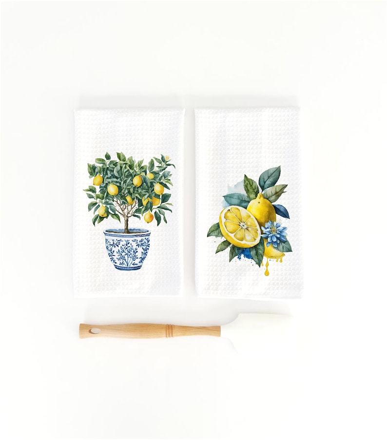 K&ouml;nnte beinhalten: Zwei wei&szlig;e K&uuml;chent&uuml;cher mit Zitronenmotiven. Ein Handtuch zeigt einen Zitronenbaum im Topf mit blauen und wei&szlig;en Details. Das andere Handtuch zeigt eine Zitronenscheibe mit gr&uuml;nen Bl&auml;ttern und einer blauen Blume.