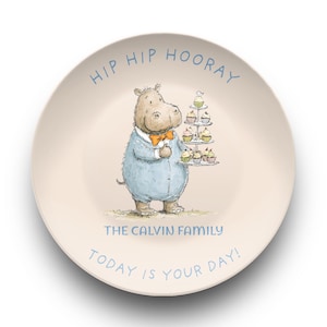 Puede incluir: Un plato redondo de color crema con una ilustración de dibujos animados de un hipopótamo con traje azul y pajarita naranja, sosteniendo un soporte para cupcakes. El texto dice HIP HIP HOORAY, THE CALVIN FAMILY, TODAY IS YOUR DAY!