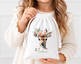 May include: A white drawstring pouch featuring a watercolor illustration of a deer with a floral crown on its head. The name Catherine is printed in green cursive script below the deer, accompanied by a small green holly leaf graphic.