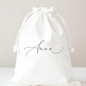 May include: White cotton drawstring bag with the name "Anna" written in black cursive script.