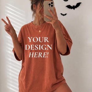 Op de afbeelding: Een oversized, roestkleurig T-shirt met de witte tekst "YOUR DESIGN HERE!" op de voorzijde. Het shirt heeft een ronde hals en korte mouwen voor een relaxte pasvorm. De stof heeft een licht vervaagde, vintage-geïnspireerde uitstraling.