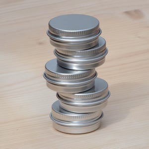 May include: A stack of six silver metal tins, each with a slightly different size and a smooth, shiny surface.