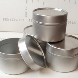 Può includere: Quattro barattoli di metallo argentati con coperchi. I barattoli sono impilati uno sopra l'altro. I coperchi sono chiusi.