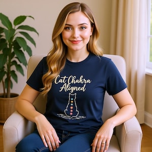Può includere: T-shirt blu navy con la scritta "Cat Chakra Aligned" e un'illustrazione di un gatto con simboli dei chakra. La maglietta è realizzata in materiale morbido, adatta per un abbigliamento casual.