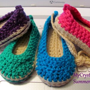 Könnte beinhalten: Vier Paar gehäkelte Babyschuhe in verschiedenen Farben: Lila, Türkis, Blau und Rosa. Jeder Schuh hat einen beigefarbenen Häkelrand. Die Schuhe sind auf einer Laptop-Tastatur angeordnet. Der Text "MyCrystalStrands Summer 2014" ist in der unteren rechten Ecke des Bildes sichtbar.