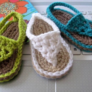 May include: Three pairs of crocheted sandals in green, white, and blue. The sandals have a brown sole and are made with a simple stitch pattern.