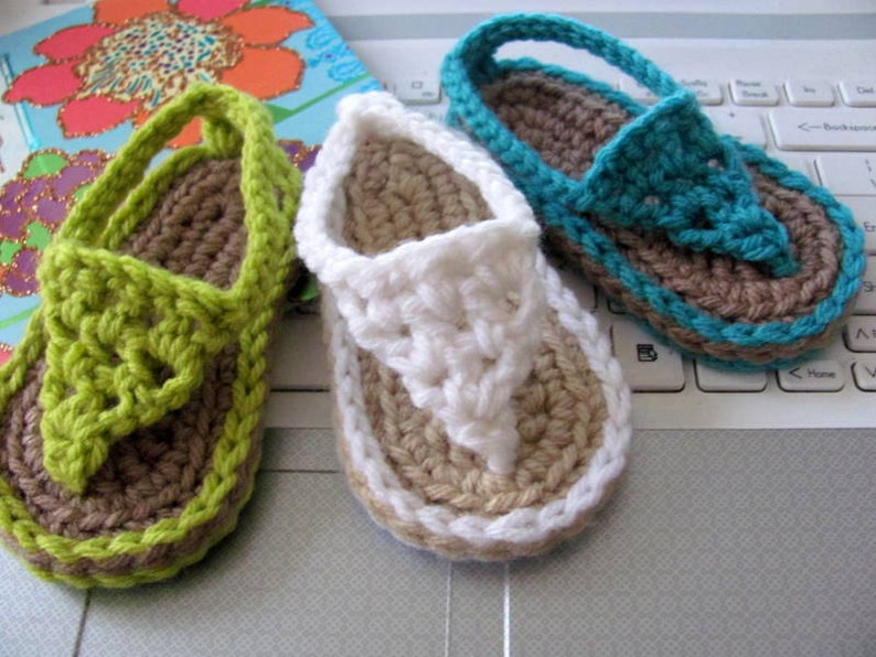 May include: Three pairs of crocheted sandals in green, white, and blue. The sandals have a brown sole and are made with a simple stitch pattern.