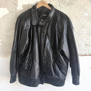 May include: A black leather jacket featuring a pointed collar, a front zipper closure, and textured panels with a subtle animal print pattern along the sleeves, shoulders, and hem. The garment includes two side pockets and a Thinsulate label.