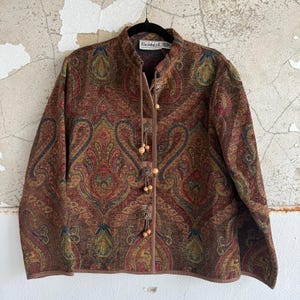 May include: A brown paisley patterned jacket with a mandarin collar and wooden button closures. The jacket has a long sleeve design and the brand name "Flashback" is visible on the label.