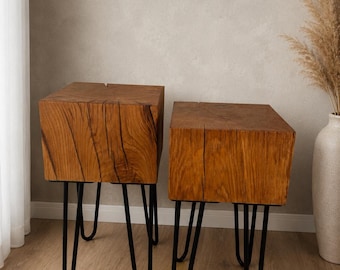 Puede incluir: Dos mesas auxiliares cuadradas con tableros de bloques de madera gruesos en tonos naturales con vetas y grietas visibles, cada una sostenida por cuatro patas de horquilla de metal negro. Las mesas están colocadas una al lado de la otra.