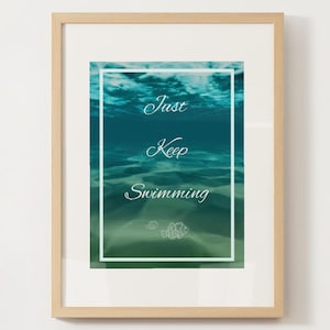 May include: Framed art print featuring an underwater scene in shades of blue and green. The text "Just Keep Swimming" is displayed in elegant script. A white border frames the image, and the frame is light brown.