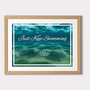 May include: Framed art print featuring an underwater scene with the text "Just Keep Swimming" in elegant script. The artwork depicts a turquoise ocean with two fish illustrations. The frame is a light brown color.