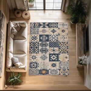 Puede incluir: Vista aérea de una alfombra estampada con fondo beige y diseños geométricos azul marino y dorado. La alfombra rectangular está colocada sobre un suelo de madera clara. La habitación incluye un sofá, plantas y una ventana.