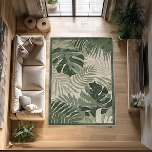 Può includere: Tappeto rettangolare con un motivo a foglie tropicali nei toni del verde e del crema. Il tappeto presenta grandi foglie di monstera e altre fronde di palma, creando un design botanico lussureggiante. Il tappeto ha un bordo verde scuro.