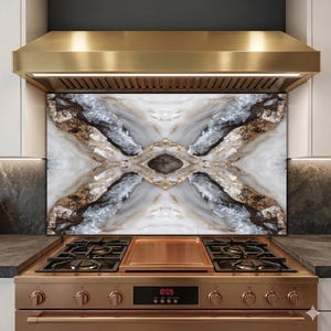 May include: A kitchen backsplash with a marble design in white, gray, brown, and gold tones. The backsplash is installed above a copper-colored stove and range hood. The stove has four burners and a digital clock displaying 10:09.