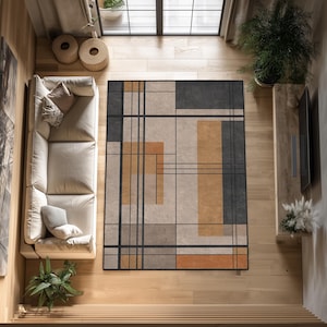 Puede incluir: Vista aérea de una alfombra rectangular con diseño geométrico. La alfombra tiene un fondo beige con formas rectangulares y lineales negras, grises y naranjas. Está sobre un suelo de madera, con un sofá blanco y plantas a la vista. Mide aproximadamente 200 cm x 300 cm.