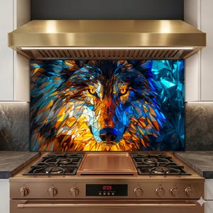 Puede incluir: Una obra de arte geométrica y colorida de la cara de un lobo, con tonos de azul, naranja y amarillo. La obra de arte está instalada como protector contra salpicaduras sobre una estufa de color cobre. Los ojos del lobo son de un amarillo brillante.