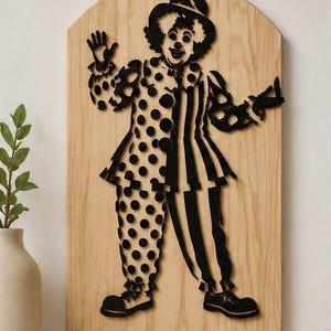 Puede incluir: Una silueta negra de un payaso montada sobre una tabla de madera clara con la parte superior arqueada. El payaso lleva un sombrero, un cuello con volantes y un traje dividido en dos patrones distintos: un lado con lunares y otro con rayas.