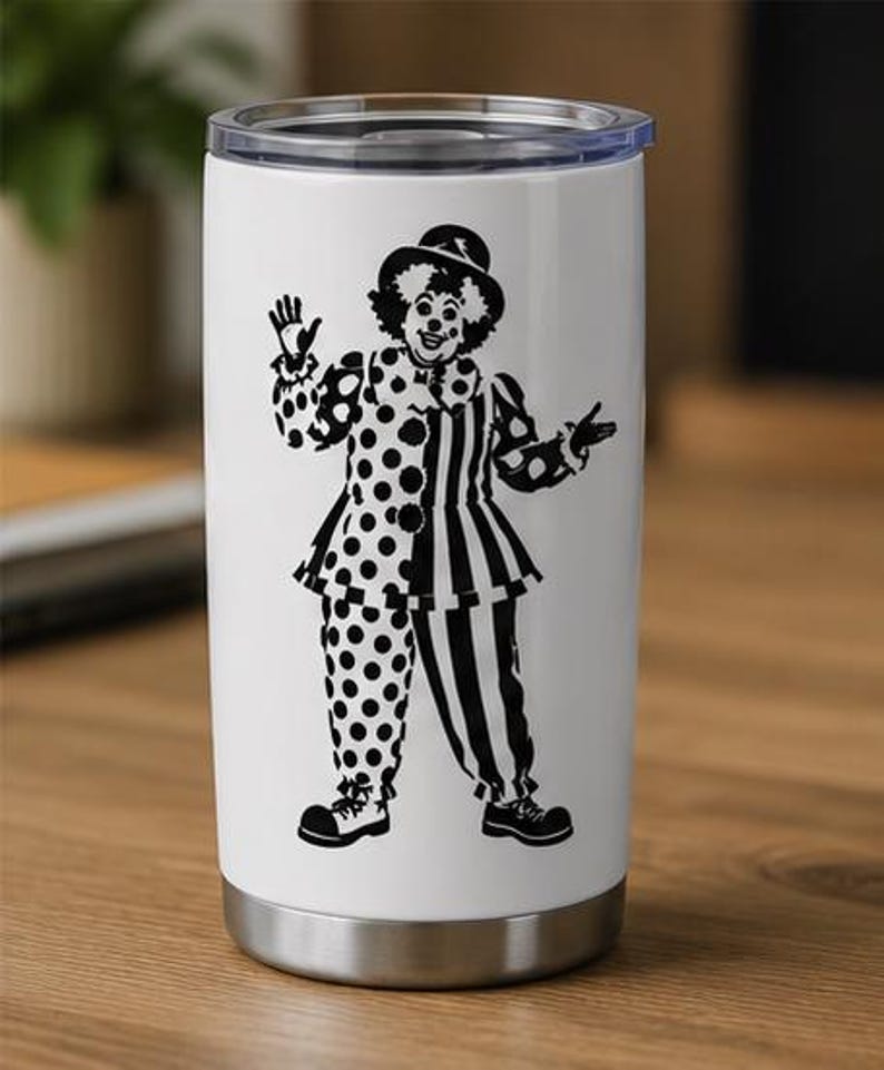 Puede incluir: Un vaso de acero inoxidable blanco con tapa de pl&aacute;stico transparente, que presenta un estampado gr&aacute;fico negro de un payaso con sombrero y un traje con un lado de lunares y el otro a rayas, de pie con los brazos extendidos.