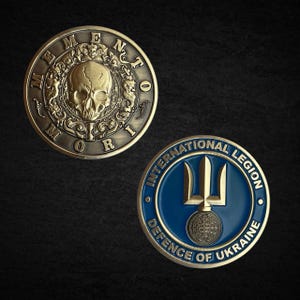 May include: Two detailed metal coins. One is bronze-colored with a skull and the words "Memento Mori". The other is blue and gold, with the words "International Legion Defence of Ukraine" and a trident symbol.