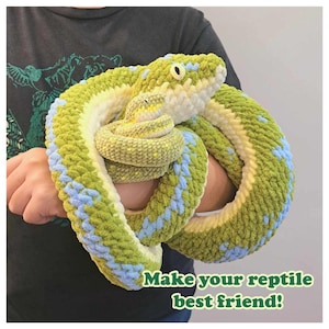 May include: A green and blue crocheted snake toy. The snake is curled up and has a small, yellow crocheted snake inside of it. The text "Make your reptile best friend!" is at the bottom of the image.