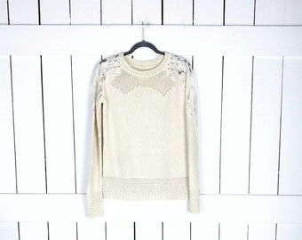 May include: A cream-colored sweater with lace detailing on the shoulders. The sweater has long sleeves and a crew neckline.