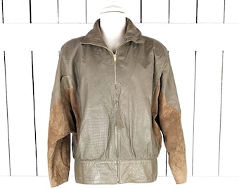 Può includere: Giacca vintage verde oliva con motivo strutturato e inserti in pelle scamosciata marrone sulle maniche. La giacca ha una chiusura con zip e un collo alto. La giacca è esposta su un manichino su sfondo bianco.