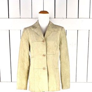 May include: A light beige suede jacket with a button closure and two pockets. The jacket is on a wooden mannequin.