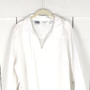 May include: White long-sleeve button-down shirt with a v-neck collar. The shirt has a relaxed fit and is made of a lightweight fabric.